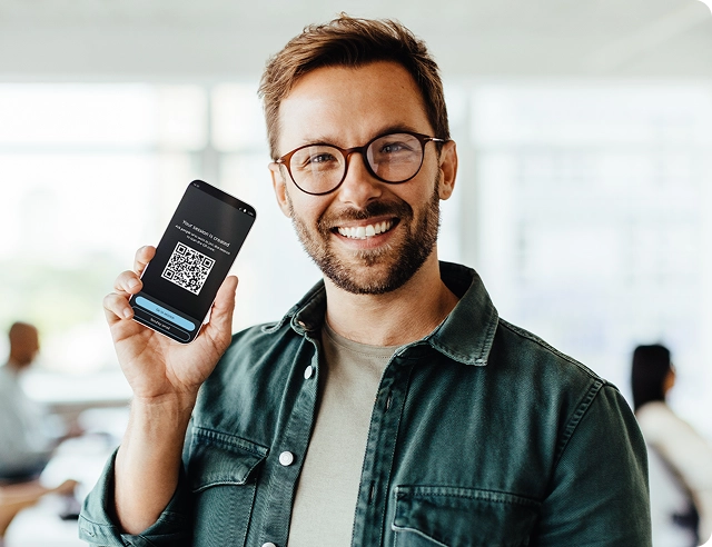 Nasmijani muškarac drži pametni telefon na kojem je prikazan QR kod za pridruživanje Vasco Audience programu.